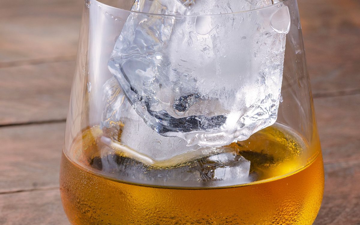 A whiskey glass with a large ice cube on a wooden table