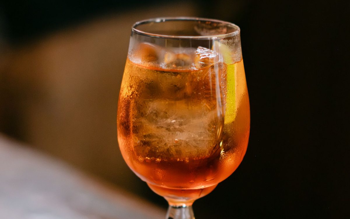 A bright orange spritz with ice and an orange slice on a wooden table