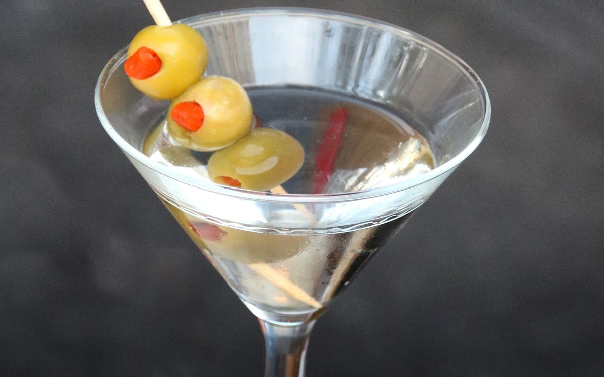 A classic martini with green olives on a glass table