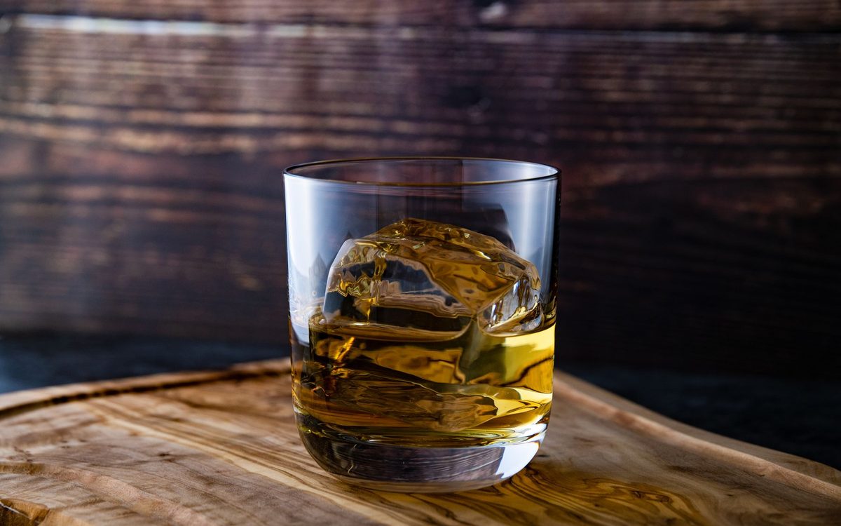 Whisky glass with a large ice cube on a wooden surface in moody light